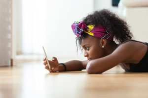 an african girl laid down on the floor and looking at her smartphone