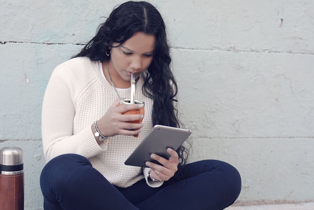 a young girl drinking mate and using its ipad