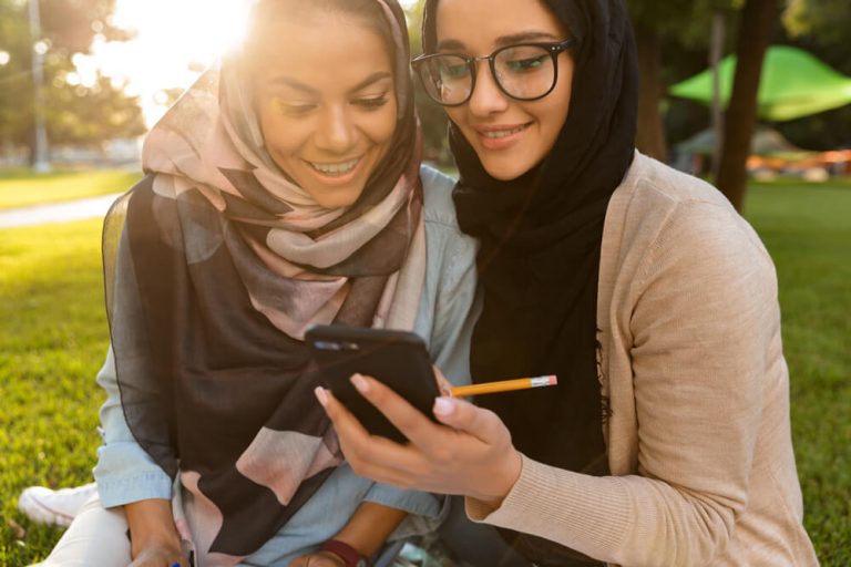 two girls sat in the park and looking at their smartphone